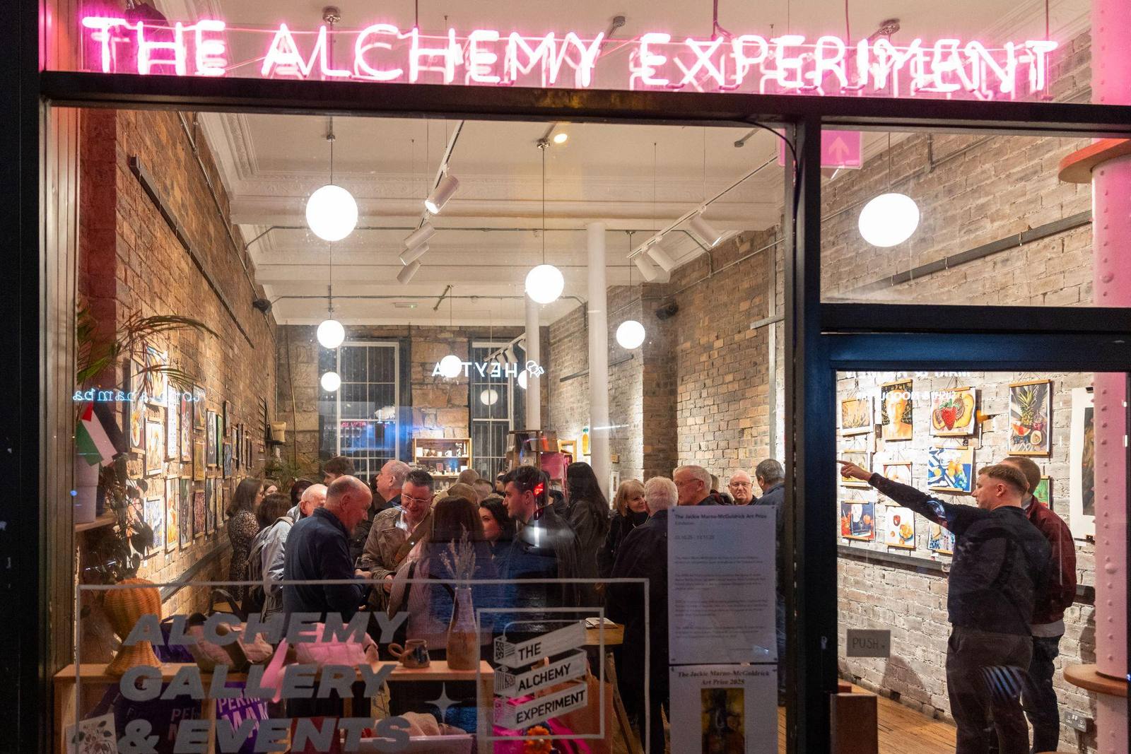 Crowds inside The Alchemy Experiment on Byres Road at the 2025 opening, seen through the window beneath the neon sign.