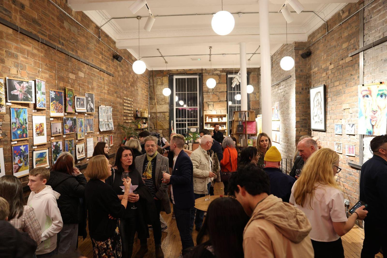 Guests filling the room at the 2024 opening night, artworks lining both walls.